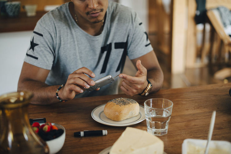 Man doing diabetes test while having breakfast at table