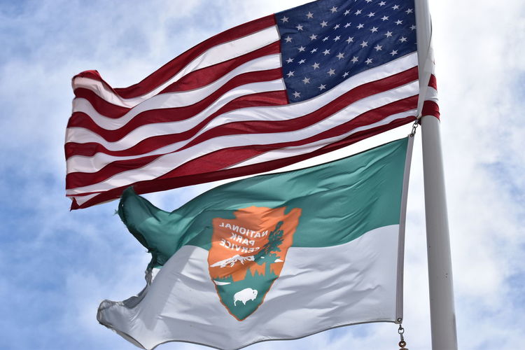 American flag and national park flag against sky