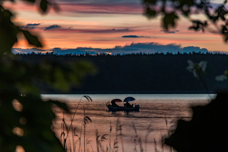 Fishing people in sea against sky during sunset