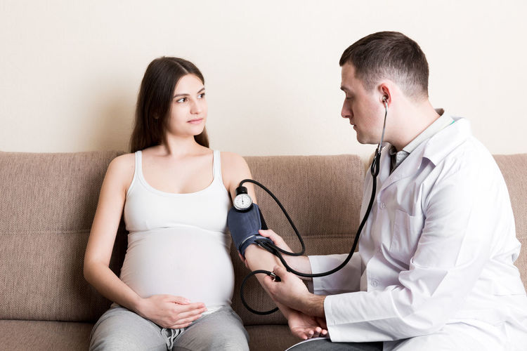 Young doctor is checking blood pressure of pregnant woman at home. high pressure problem 