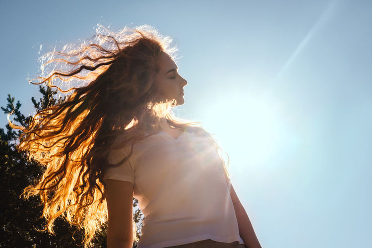 Low angle view of girl tossing hair against sky