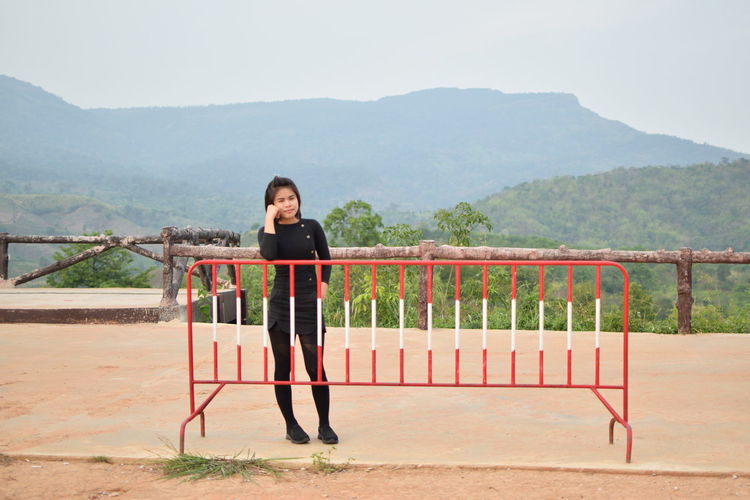 Full length portrait of woman standing by railing against mountains