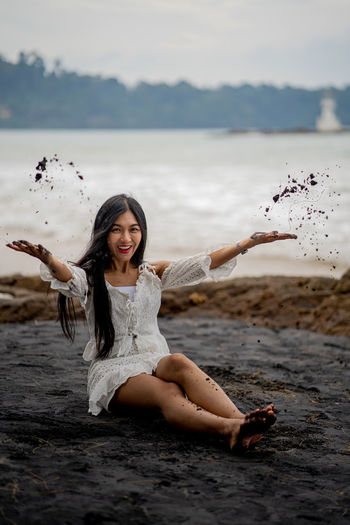 Portrait of young woman playing with black sand at beach