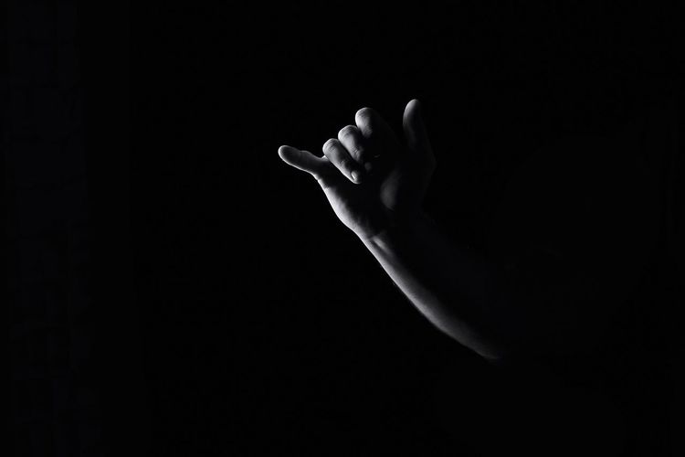 Cropped image of hand gesturing shaka sign against black background