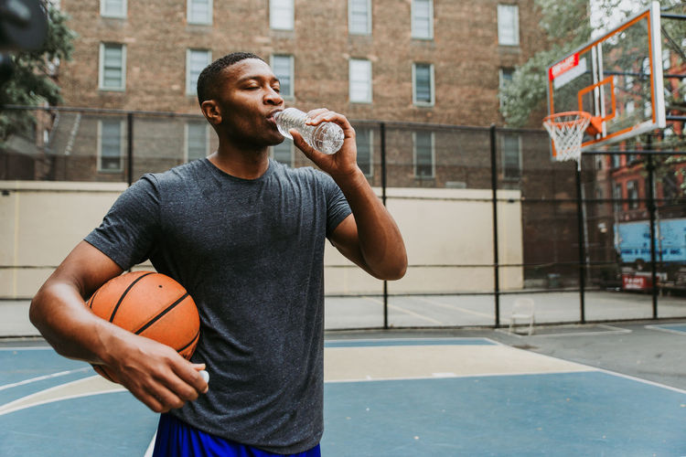 Male athlete holding basketball while drinking water in court