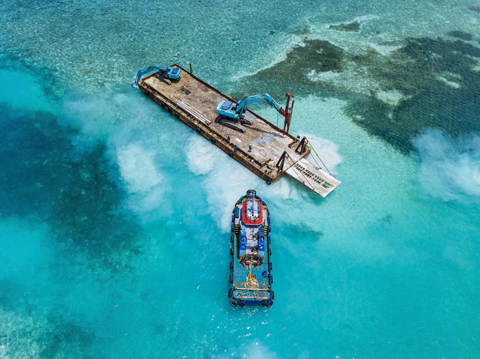 Aerial view of earth movers handling poles on floating platform in male atoll
