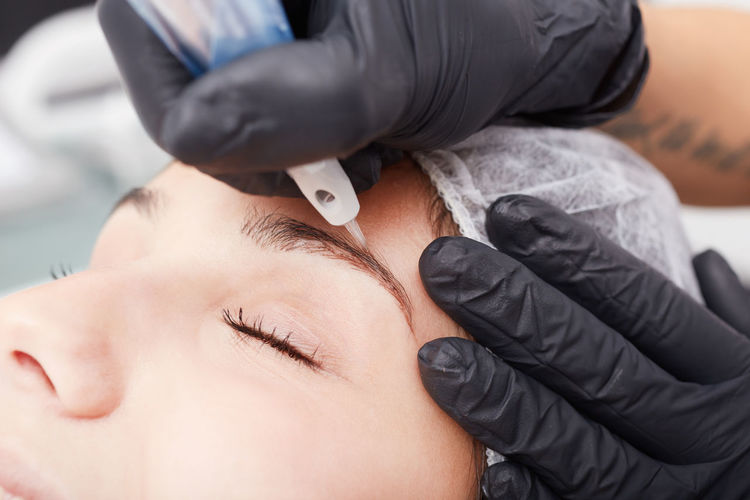 Cropped hands of beautician treating woman permanent eyebrow