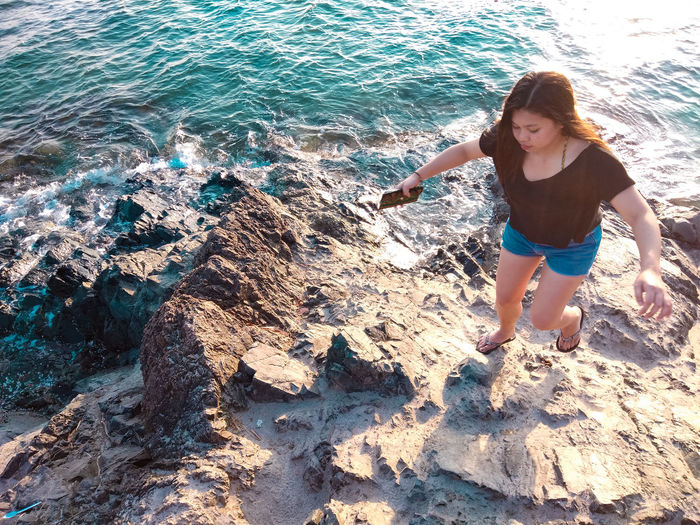High angle view of young woman walking on rock at beach