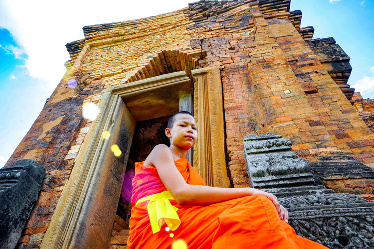 Low angle portrait of teen monk sitting outside temple