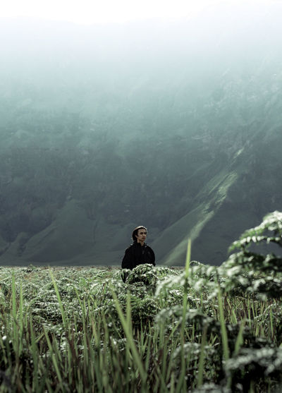 Man sitting on field against mountains