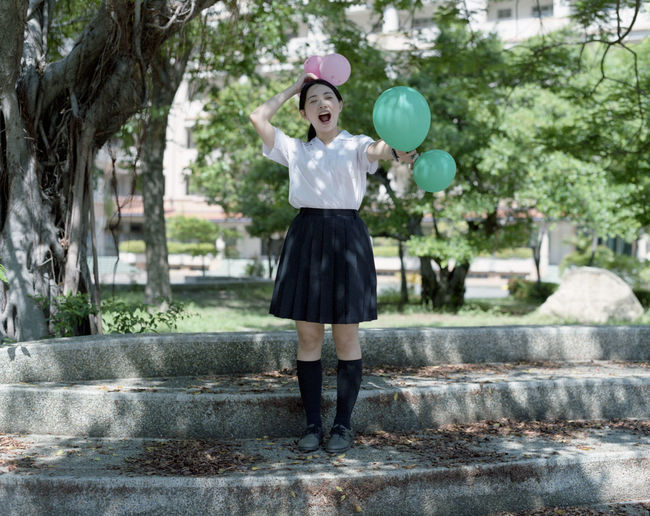 Happy woman with balloons standing on steps in park
