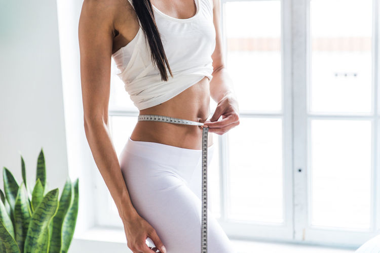 Midsection of woman measuring waist at home