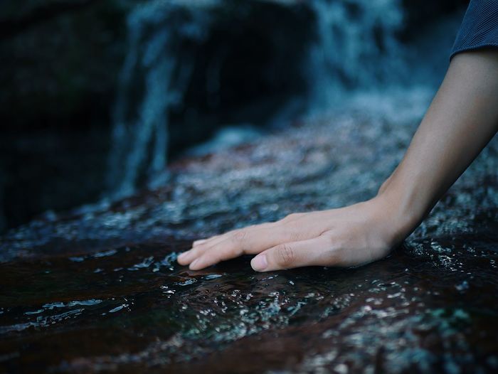 Close-up of person hand on wet rock