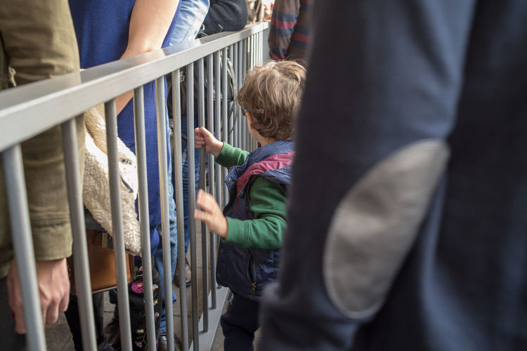 Boy standing by railing amidst crowd in city
