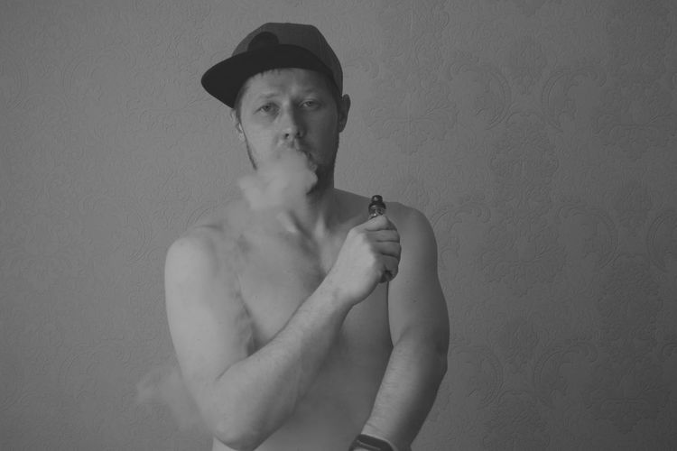 Portrait of young man smoking against wall