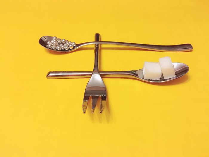 High angle view of sugar cubes and pearls in spoons on yellow background