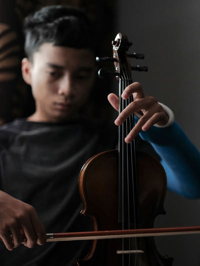 Midsection of a young man trying to play the violin with  his casted left injured hand