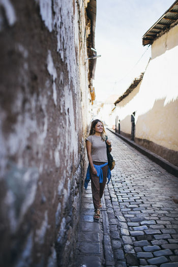 A young woman is standing near an old wall in cusco, peru