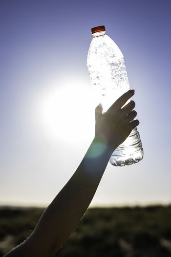 Close-up of hand holding bottle against sky on sunny day