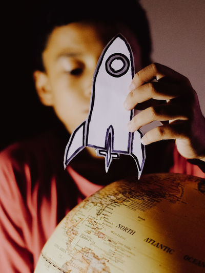 Close-up of boy playing a space ship card next to a earth globe