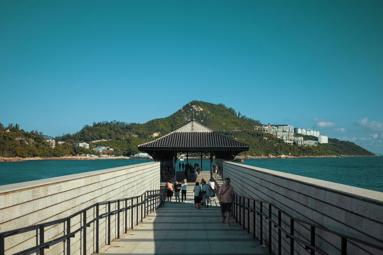 People on pier over sea against blue sky