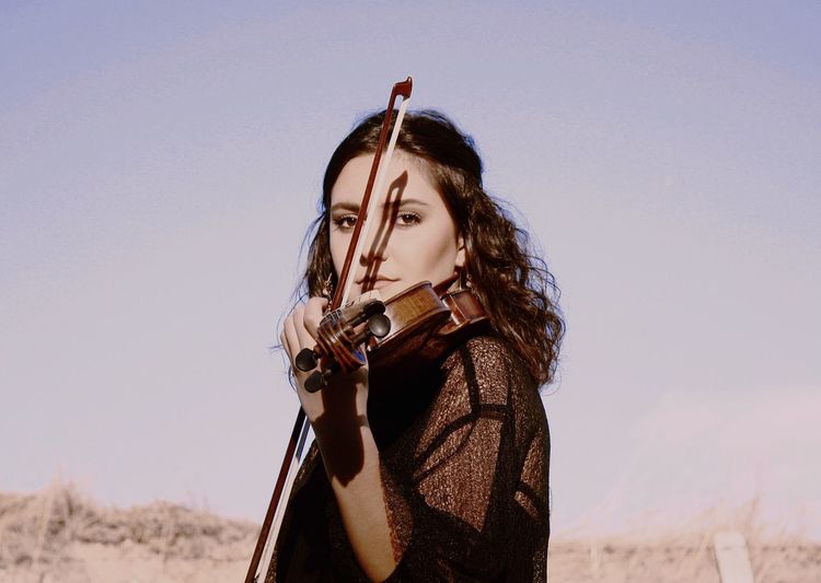 Portrait of young woman playing violin against clear sky