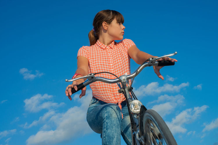 Low angle view of girl riding bicycle against blue sky