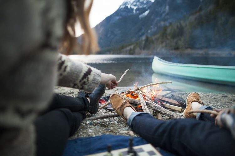 Low section of couple sitting by burning campfire at silver lake provincial park