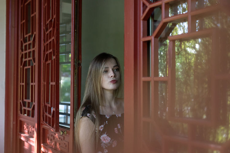 Portrait of woman standing against window at home