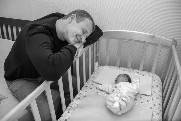 Baby in crib while happy man sitting on bed at home