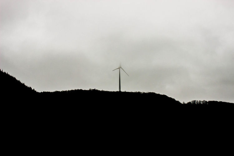 Silhouette of wind turbine against cloudy sky