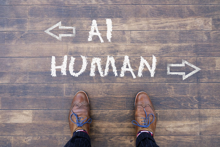 Man looking down at the words artificial intelligence - ai - and human chalked onto the floor