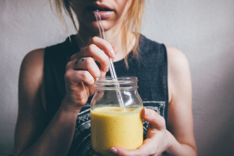 Midsection of woman drinking smoothie against wall