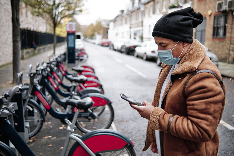 Latino man wearing a face mask checking his phone outdoors
