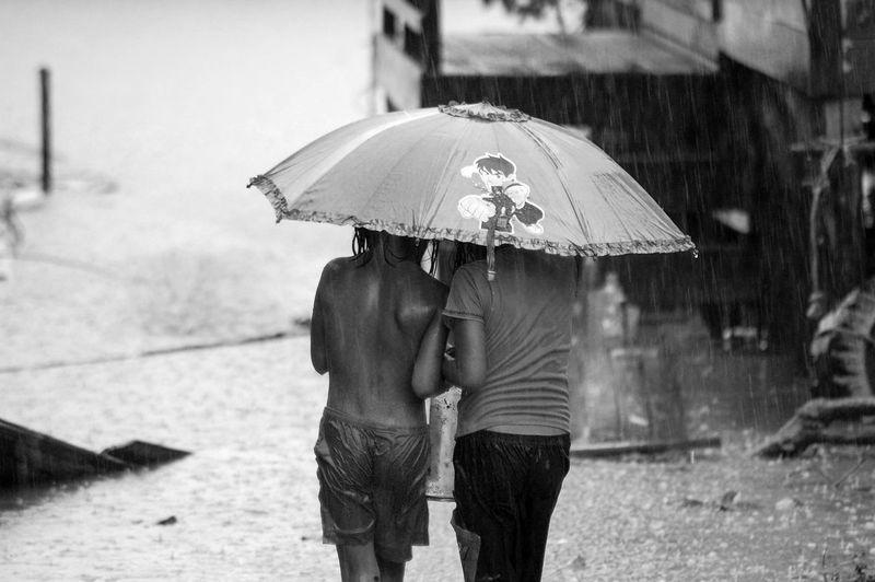 Rear view of boy and girl with umbrella walking on street during rainy day