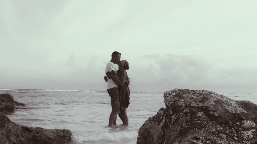 Couple kissing while standing in sea against sky