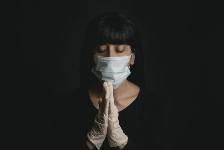 Woman wearing mask praying against black background
