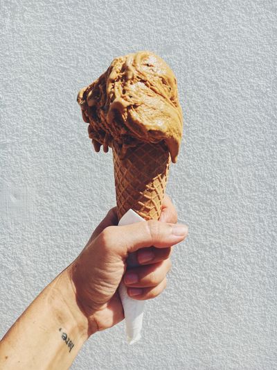 Cropped hand holding ice cream against wall on sunny day