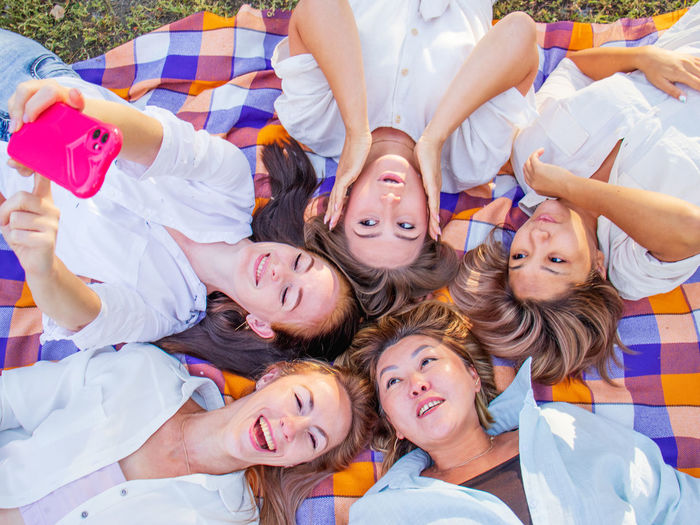 Picnic in nature, positive women lie on a blanket on the grass and take a selfie