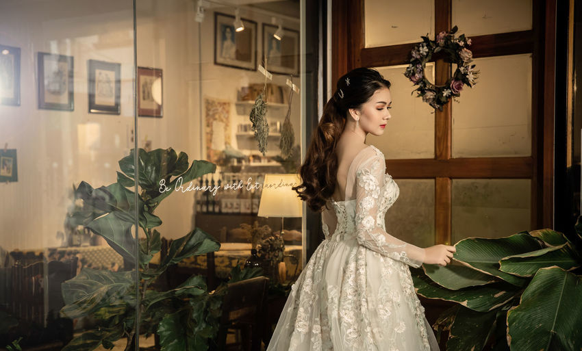 Woman wearing wedding dress while standing glass door