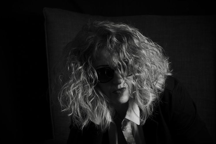 Close-up portrait of woman with frizzy hair against black background