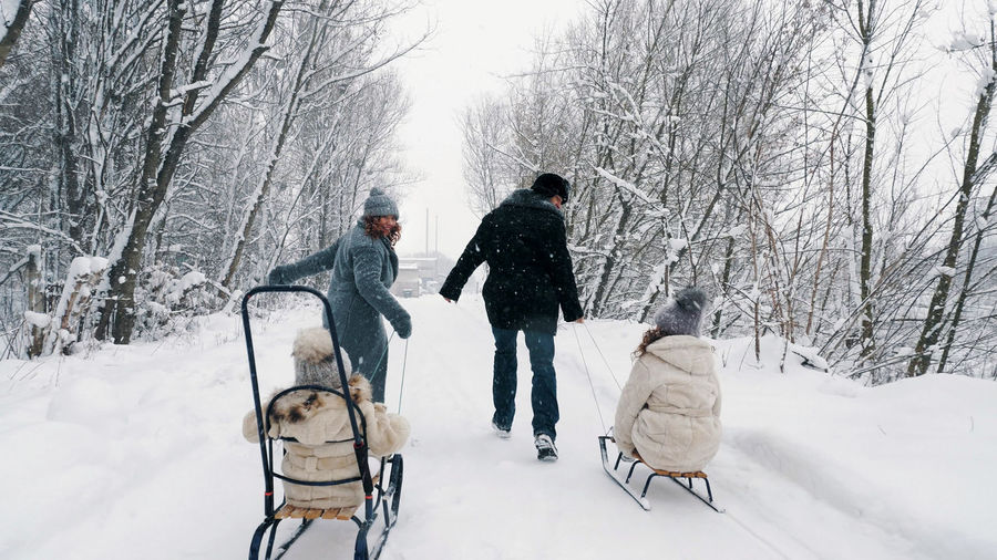 Winter  happy, laughing, playful family of 4 is enjoying of sledging their children on snowy road