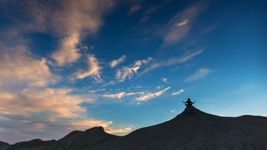 Low angle view of person sitting on mountain against sky