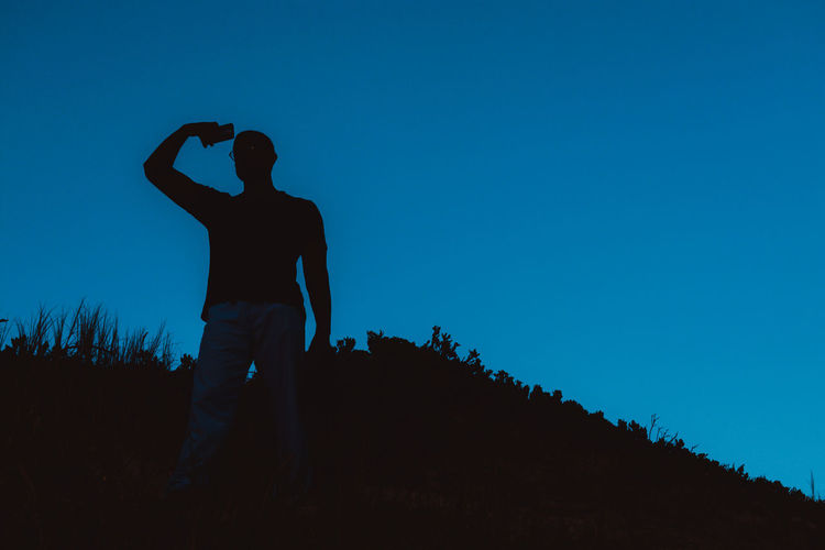Silhouette man standing on field against clear blue sky