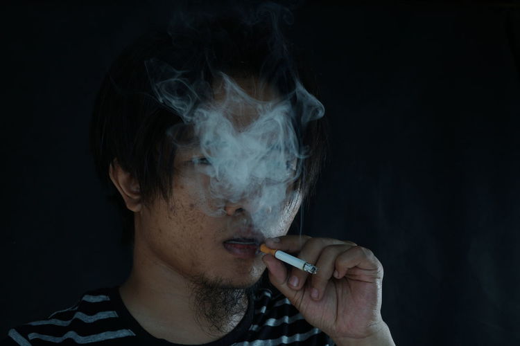 Close-up of young man smoking cigarette against wall