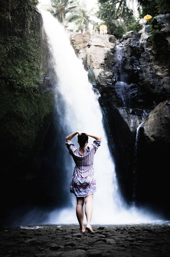 Full length of young woman standing against waterfall