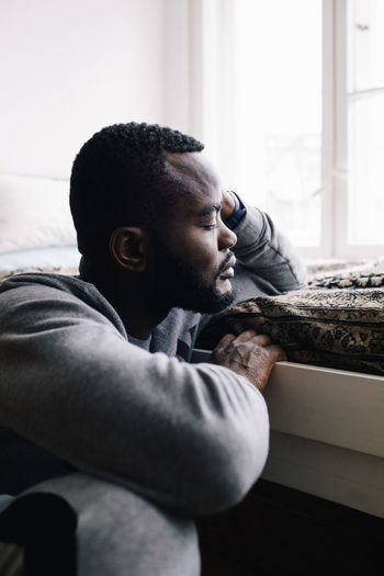 Depressed man contemplating while leaning on bed at home