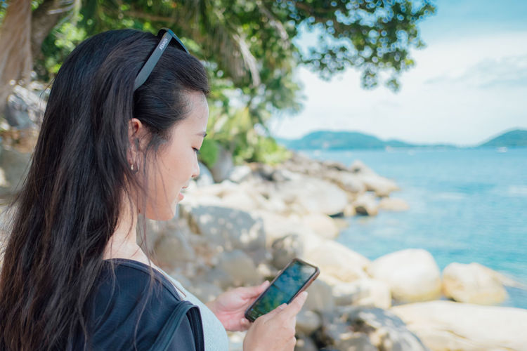 Young woman using mobile phone while sitting at beach