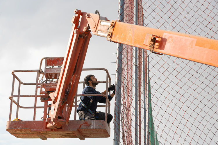 Low angle view of man working on crane outdoors
