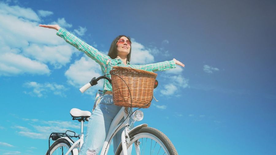 Low angle view of young woman with bicycle against sky